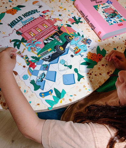 Fille assemblant le puzzle coloré 48 pièces "Hello Hossy House" sur une table – vue du dessus – Hello Hossy